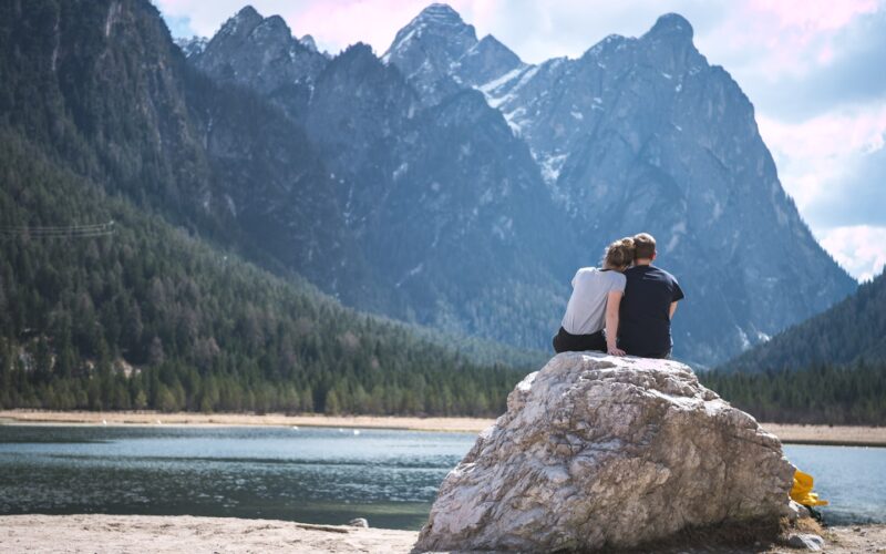 a couple sits on a rock looking out over a lake