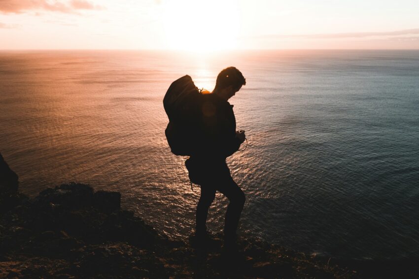 silhouette photo of man standing on rock near body of water