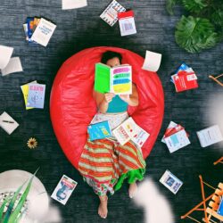 woman lying on red beanbag chair reading book