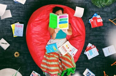 woman lying on red beanbag chair reading book