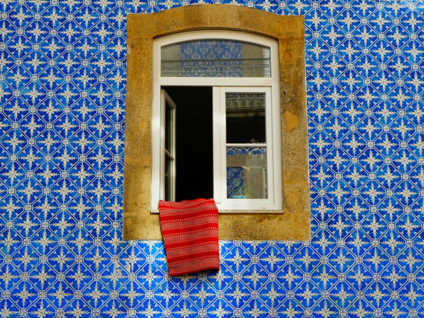 A classic Portuguese window framed by vibrant azulejo tiles featuring intricate blue and white patterns.