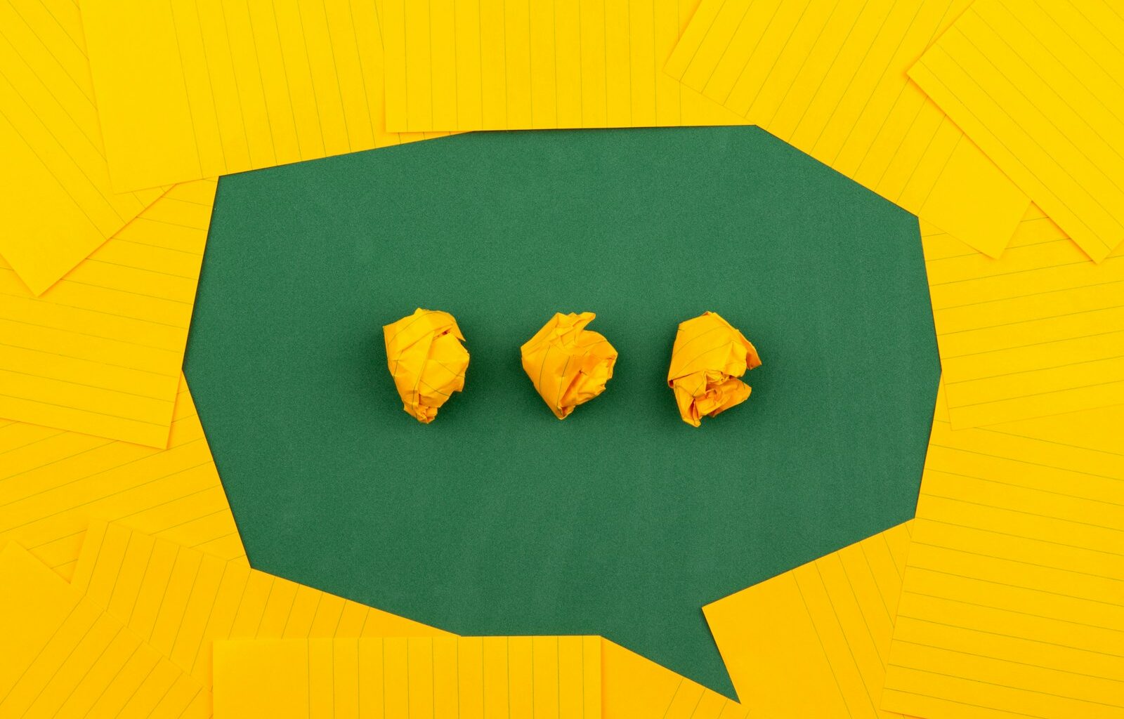 three crumpled yellow papers on green surface surrounded by yellow lined papers