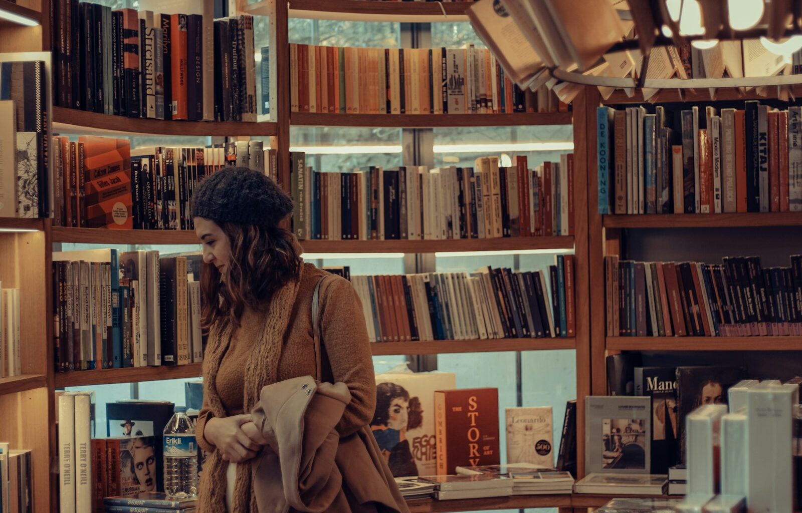 woman in brown coat reading book in library