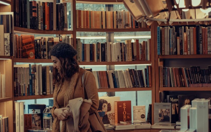 woman in brown coat reading book in library