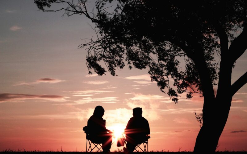 silhouette of two person sitting on chair near tree