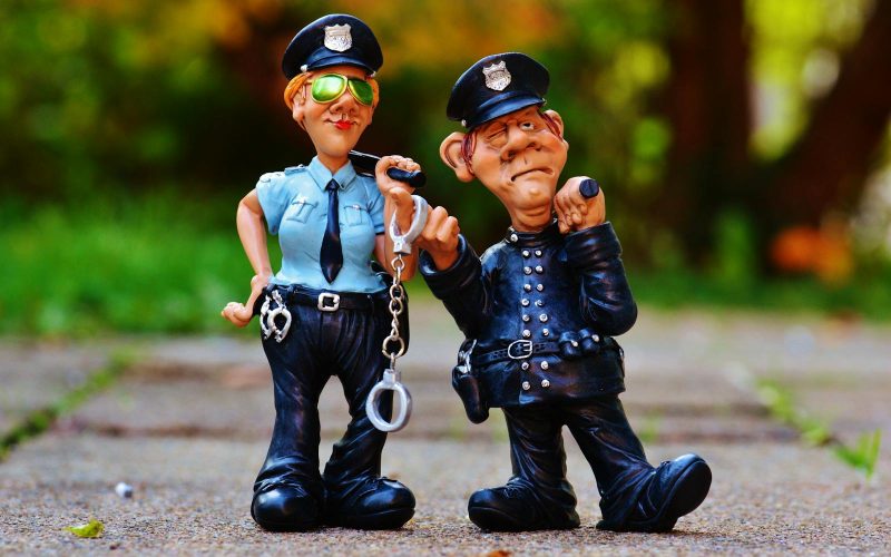 Two playful police figurines, complete with handcuffs and batons, depicted in a comical outdoor setting.